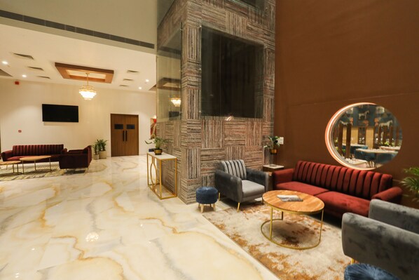 A spacious lobby with a marble floor, a red sofa, a grey armchair, and a round mirror reflecting the room.