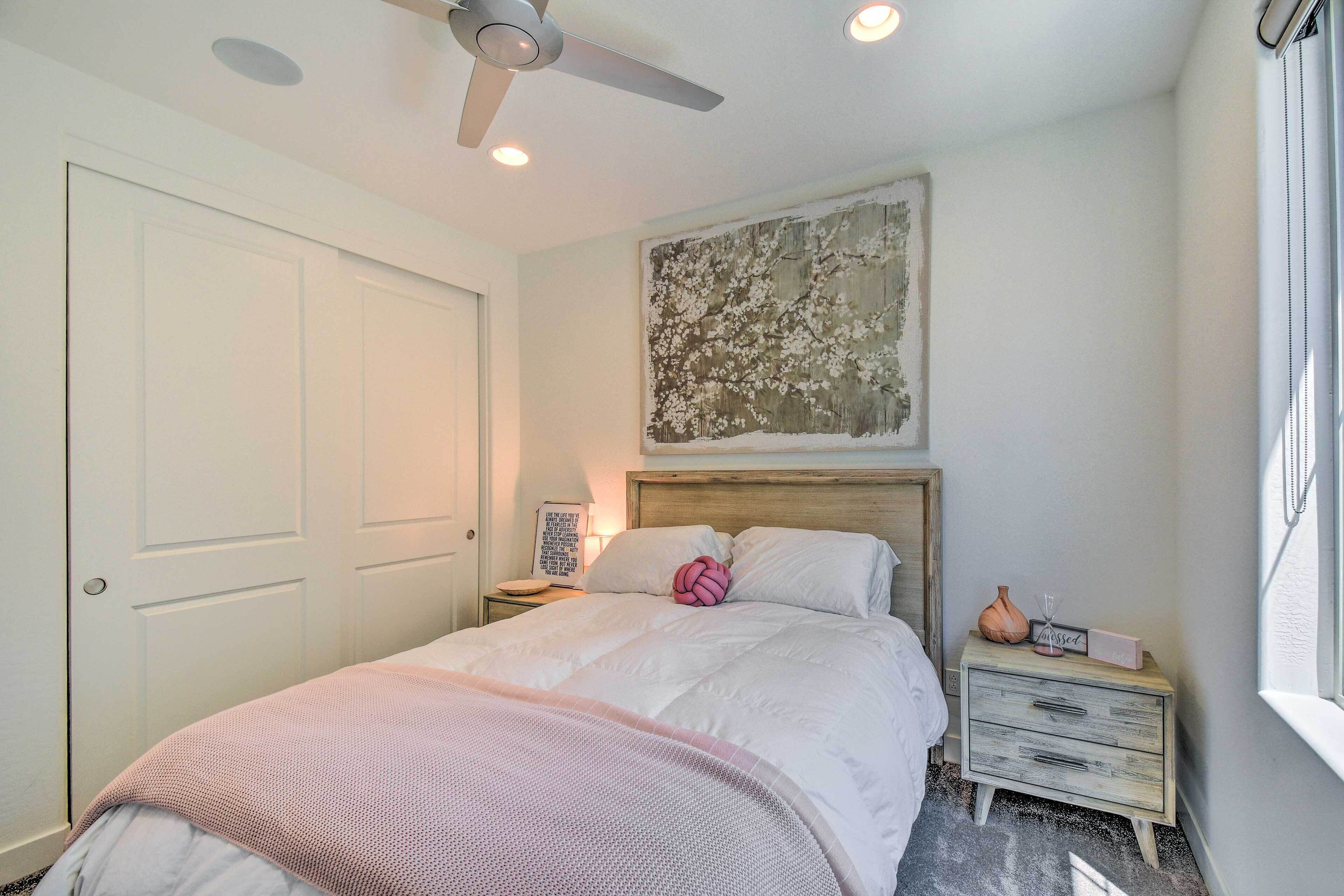 A bedroom with a bed, a nightstand, a ceiling fan, a wall art piece, and a window.