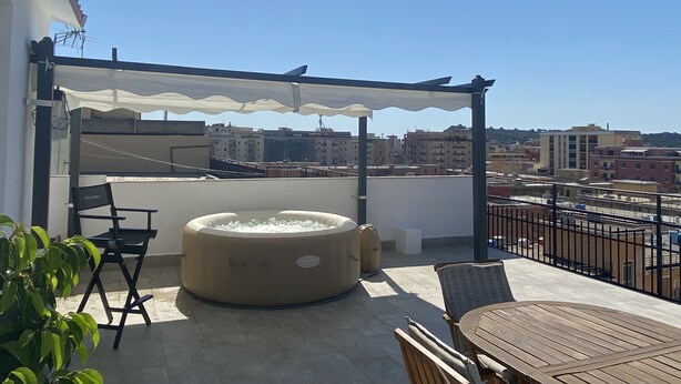 A rooftop terrace with a covered seating area, a hot tub, and a view of the cityscape.