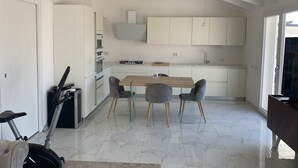 A modern kitchen with white cabinetry, a wooden dining table, and a built-in stove.