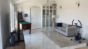 A living room with a pool table, a sofa, an exercise bike, and a bookshelf.