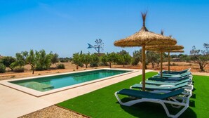 Una piscina con sillas de descanso y un quiosco techado de paja.