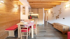Un intérieur en bois comprenant une table à manger, des chaises, un banc et un coin cuisine.