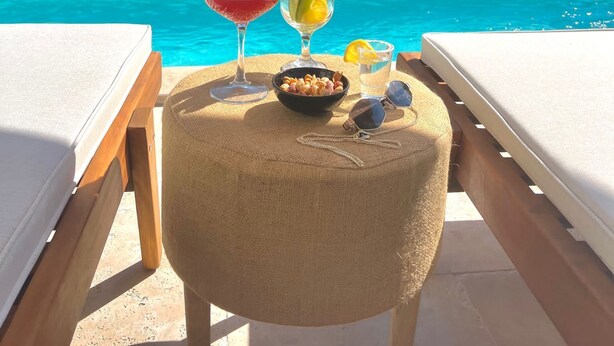 Escena junto a la piscina con valla de madera, sillas de descanso y una mesa con bebidas y aperitivos.