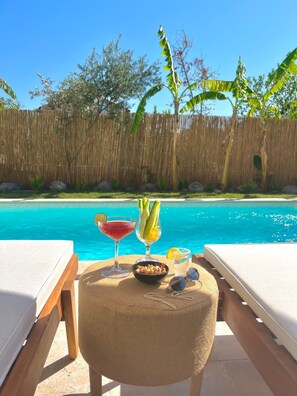 A poolside setting with a wooden fence, lounge chairs, and a table with a drink and snacks. - Myrodia by Etapaltınel (Ayvalik)