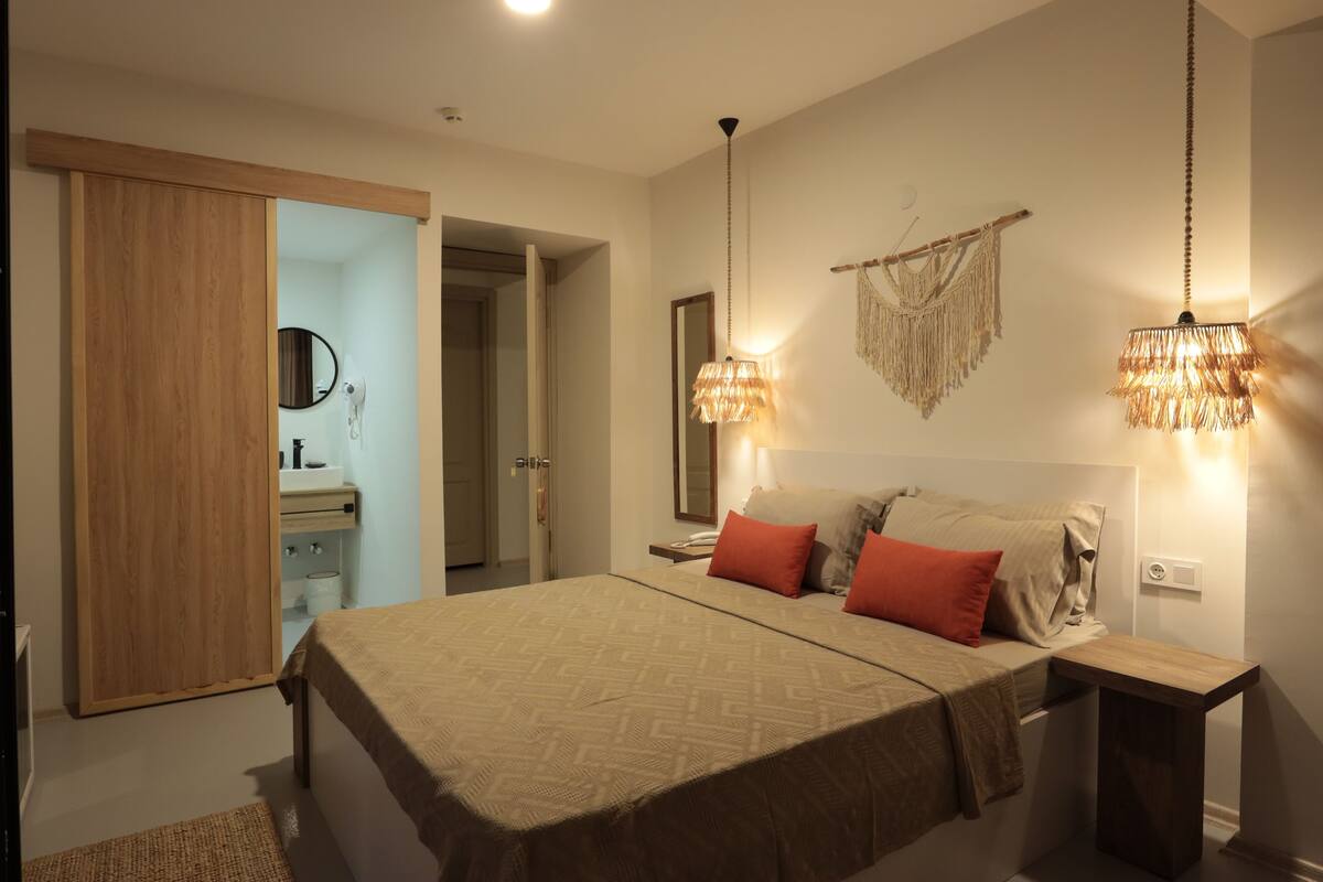 A bedroom with a bed, bedside tables, a mirror, and a hanging light fixture.
