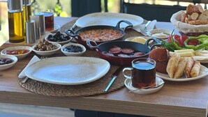 Una mesa servida con varios platos, salsas y bebidas en un balcón con vistas a un paisaje urbano.