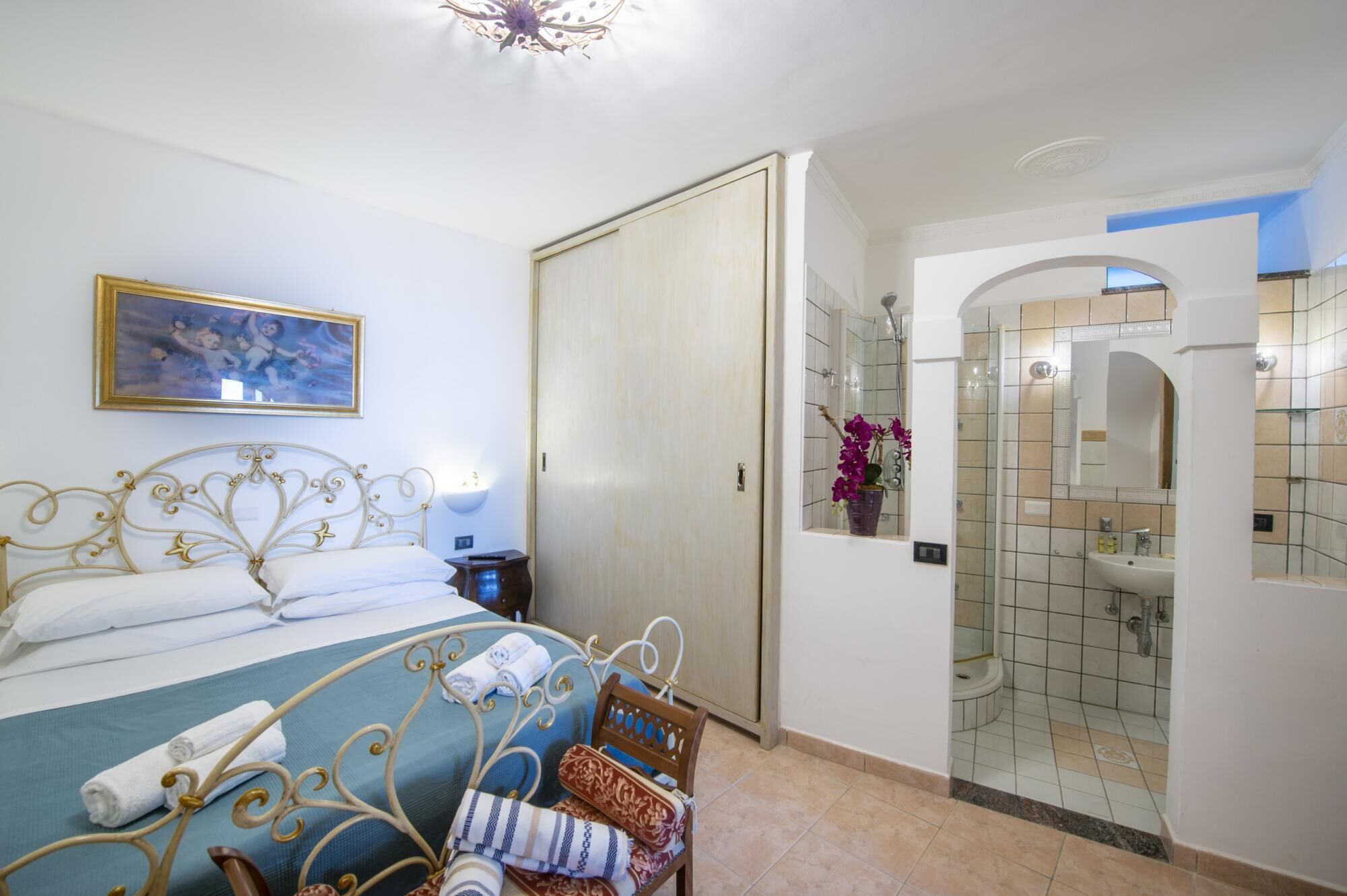 A hotel room with a bed, a nightstand, a wardrobe, and a bathroom with a shower and sink.