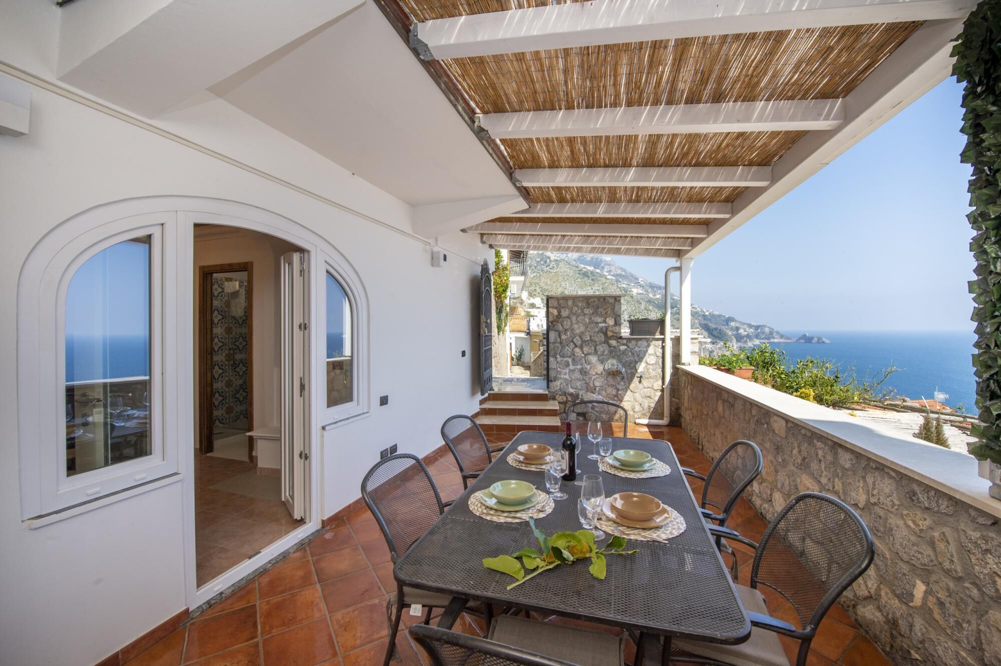 A terrace with a table set for dining, overlooking a coastal view.