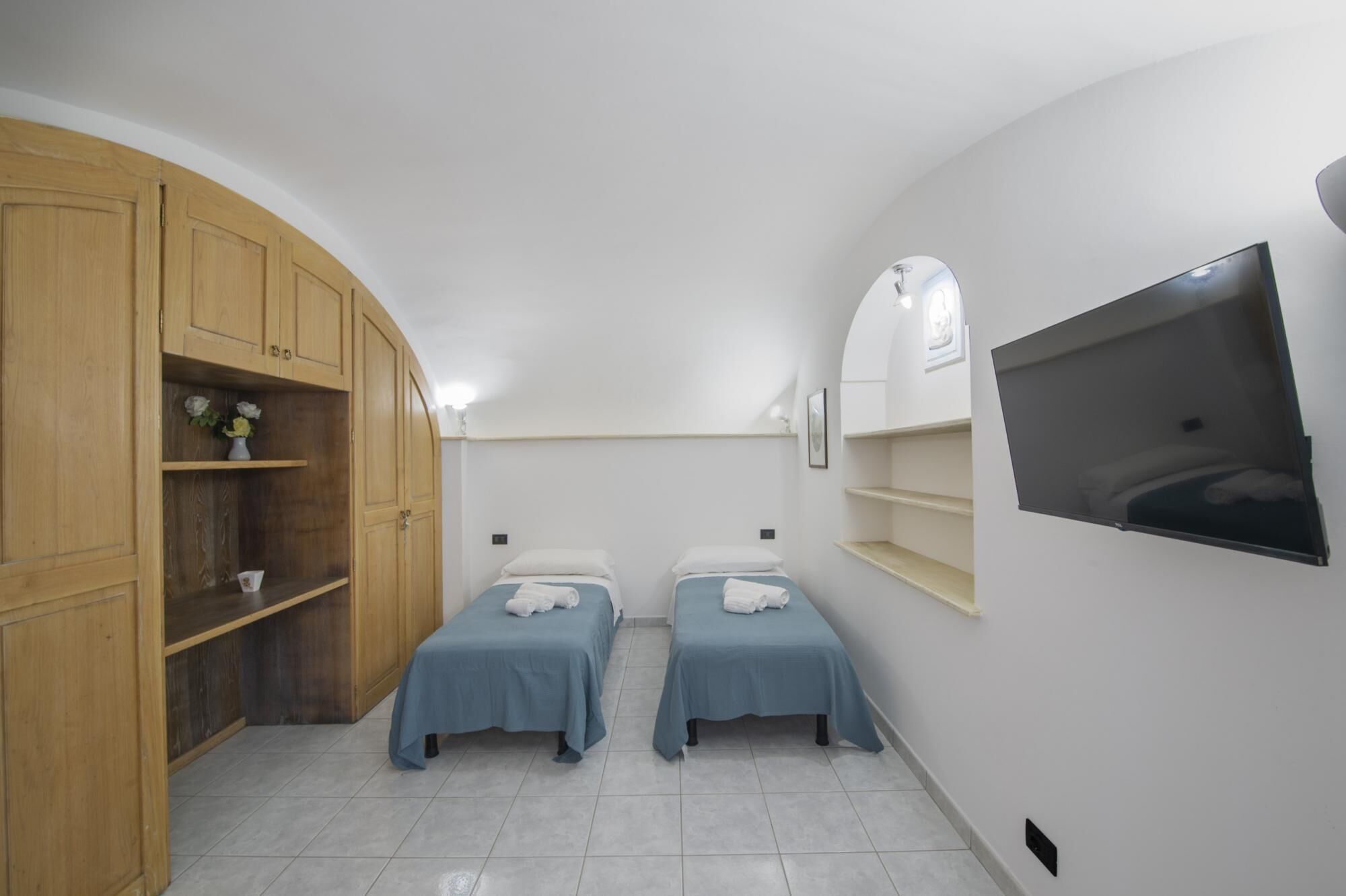 Una habitación con dos camas, armarios de madera, un televisor y suelo de baldosas.