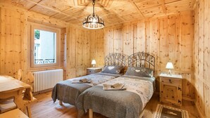 Une chambre dans un chalet en bois, avec deux lits, une table, un radiateur et une fenêtre.