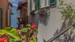 A narrow street with buildings on either side, a balcony with flowers, and a view of the sea. - Casa Greppi Varenna in Varenna (Varenna)