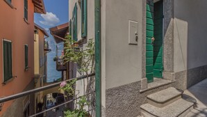 A narrow street with buildings featuring green shutters and a visible water body in the background. - Casa Greppi Varenna in Varenna (Varenna)