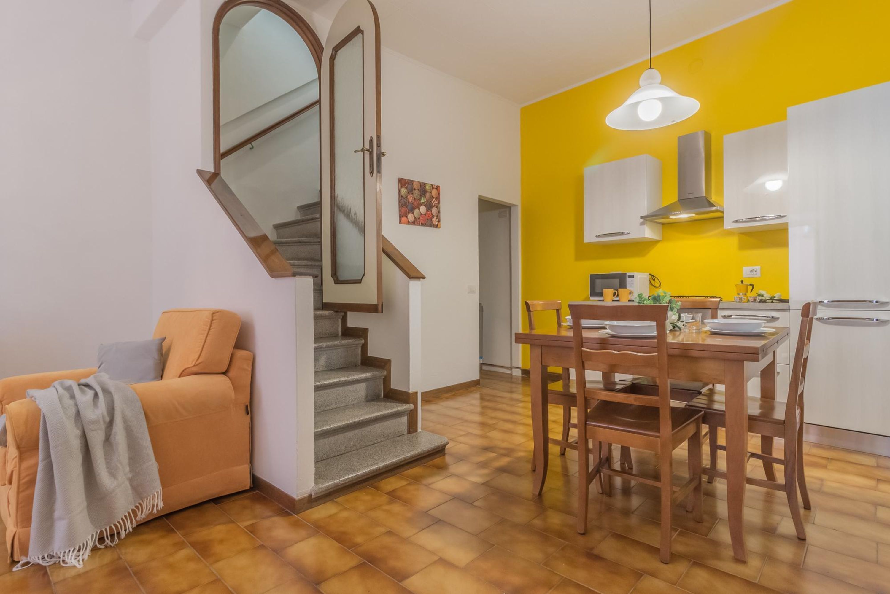 Un apartamento moderno con una escalera, un comedor con sillas de madera y una cocina con armarios blancos.