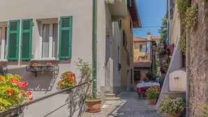 A narrow street with buildings on either side, featuring balconies with potted plants and a staircase leading to a second floor. - Casa Greppi Varenna in Varenna (Varenna)
