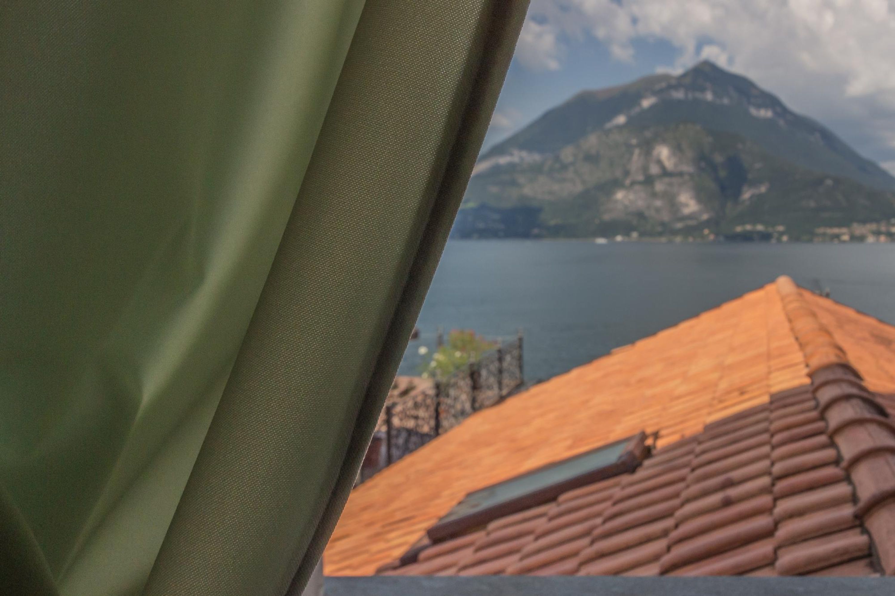 A view of a mountain and a body of water from a window with a green curtain.