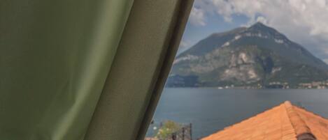 A view of a mountain and a body of water from a window with a green curtain.
