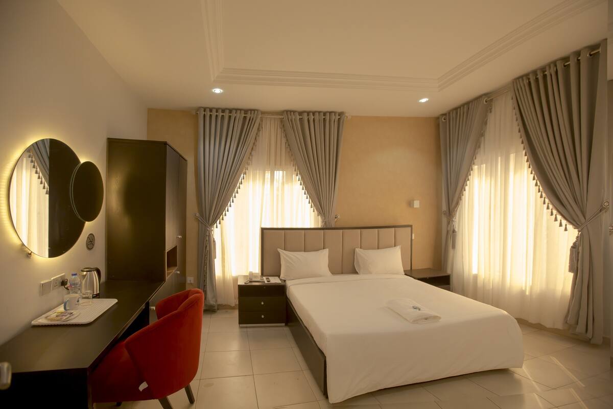 A hotel room with a bed, a desk, a chair, a wardrobe, and curtains.