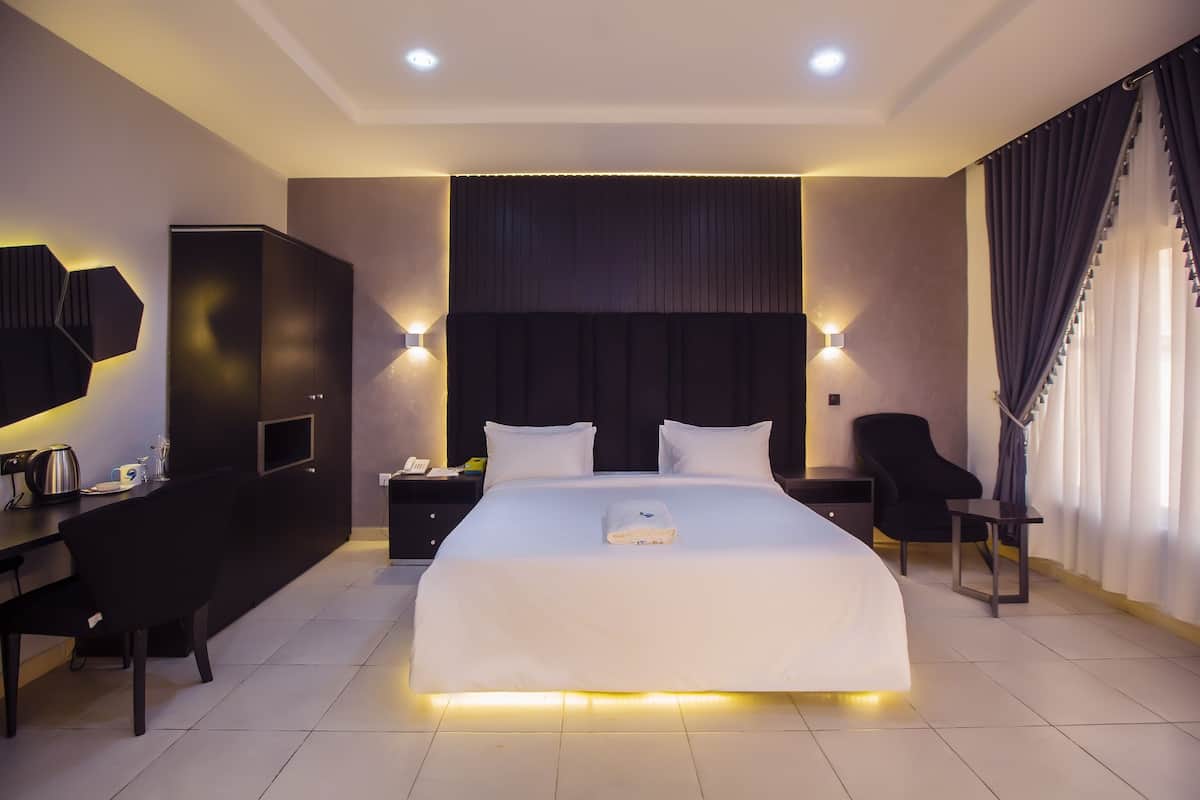 A modern hotel room with a large bed, a desk, a chair, and a wardrobe.