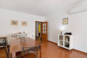 A dining area with a wooden table and chairs, a white bookshelf, and a door leading to another room.