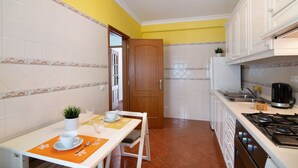 A kitchen with white cabinets, a wooden door, a dining table with a plant, and a coffee maker. - Apartment 'Algarvio Ao Sol' with Balcony, Wi-Fi and Air Conditioning (Conceição de Tavira)