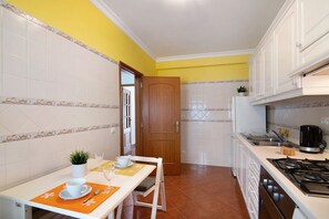 A kitchen with white cabinets, a wooden door, a dining table with a plant, and a coffee maker.