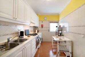 A kitchen with white cabinets, a stove, a sink, and a small dining table with a chair.