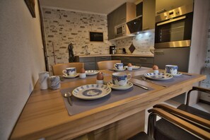 Un comedor con una mesa de madera preparada para cuatro personas, con platos, tazas y cubiertos.