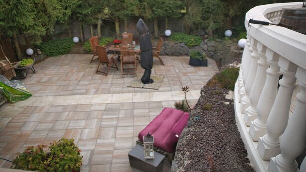 Un patio con mesa y sillas, rodeado de follaje y un muro de piedra.