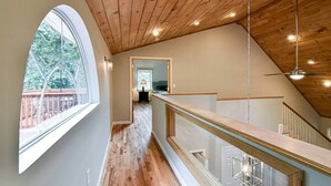 Ein Holzinnenraum mit hoher Decke, einer Treppe und Blick durch ein großes Fenster.