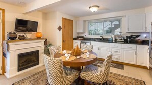 A dining area with a round table, zebra-striped chairs, a fireplace, and a television on the wall. - Ramblin Rose, Apartment in Central Area, Sleeps 4 (Sequim)