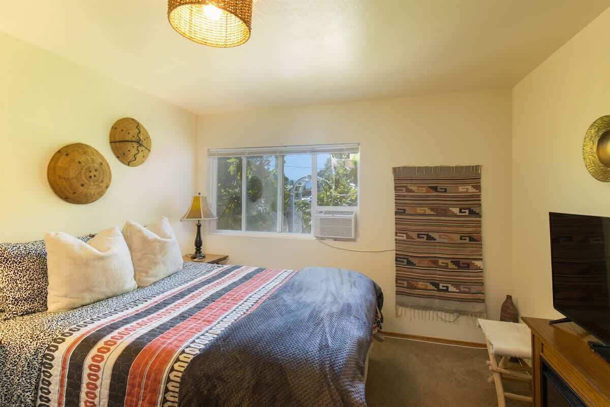 A bedroom with a bed, a TV, a window, and a wall-mounted air conditioner.