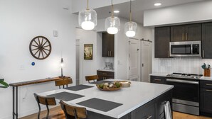 Une cuisine moderne dotée d’un îlot central, de meubles de couleur sombre, d’appareils électroménagers en acier inoxydable et de luminaires suspendus.