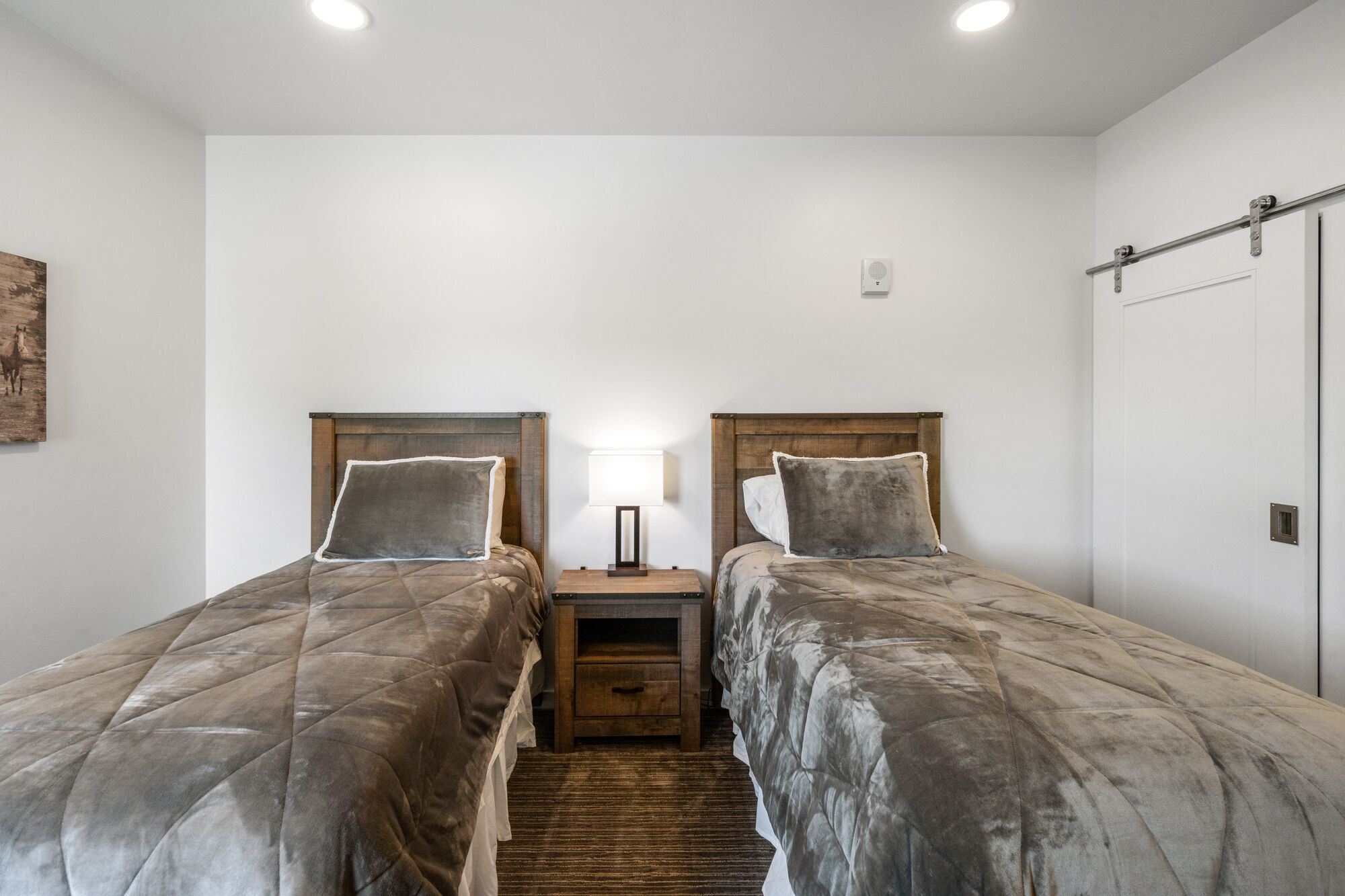 A bedroom with two beds, a nightstand, a lamp, and a door.