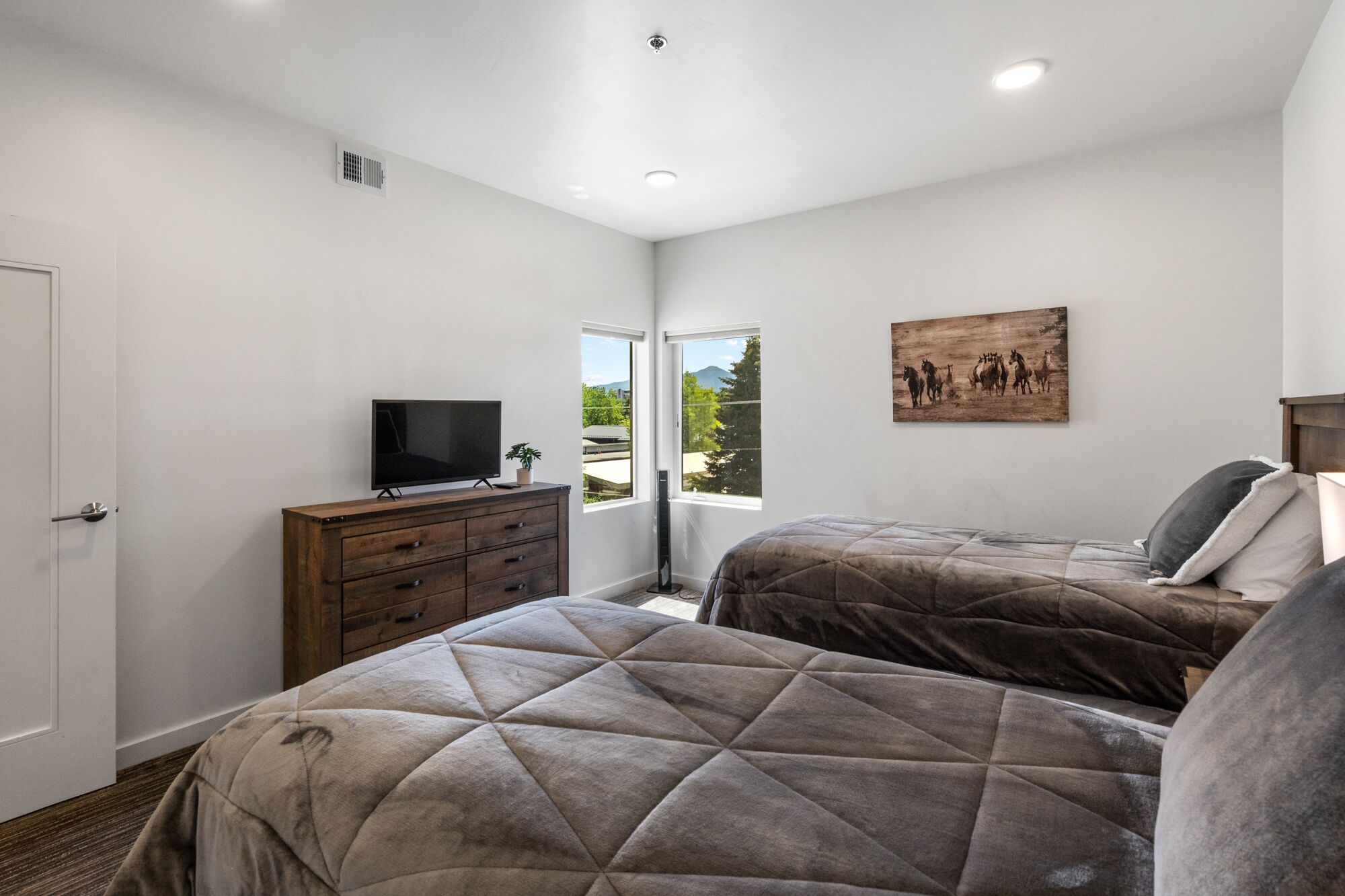 A bedroom with two beds, a TV on a dresser, and a painting on the wall.
