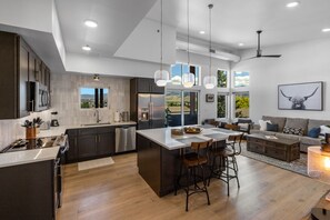 Una cocina moderna con una isla grande, armarios oscuros y vistas al exterior.