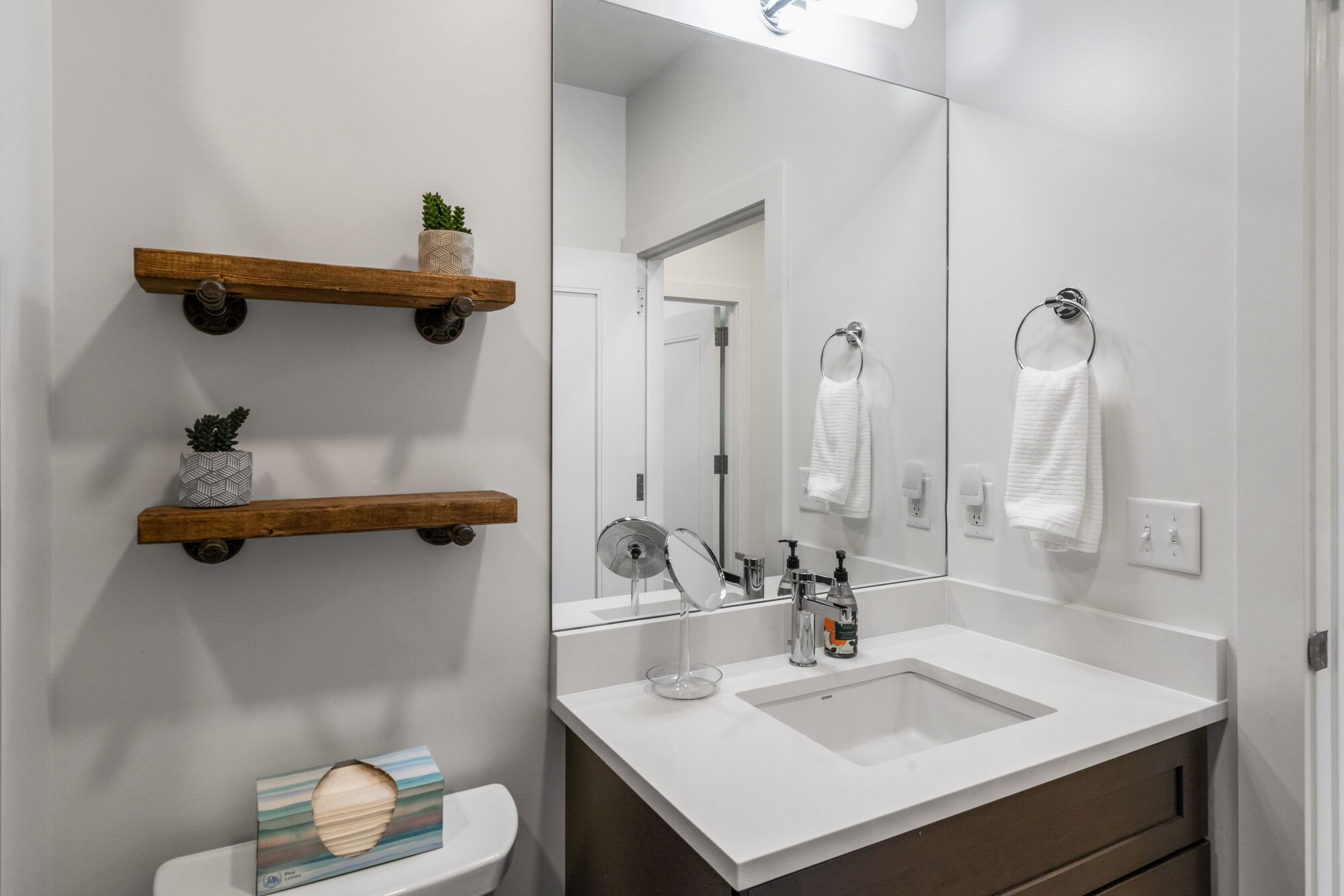 A modern bathroom with a white sink, a large mirror, and wooden shelves with decorative items.