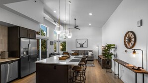 Une cuisine moderne dotée d’un îlot central, d’appareils électroménagers en acier inoxydable et de luminaires suspendus.