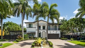 Una casa moderna a due piani con vialetto lastricato, circondata da palme e curato giardino.