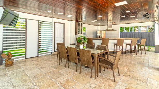 Un'ampia sala da pranzo con un tavolo grande e sedie in vimini, angolo cottura con frigorifero e fornello, e soffitto con faretti e ventilatore.