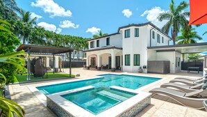Una casa a due piani con piscina, area salotto all'aperto e palme.