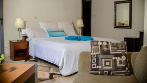 A bedroom with a bed, two bedside tables, a nightstand, a chair, a sofa, a mirror, and a rug. - ONE CLICK HOTEL (Kigali)
