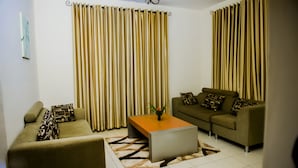 A living room with a sofa, a coffee table, and curtains. - ONE CLICK HOTEL (Kigali)