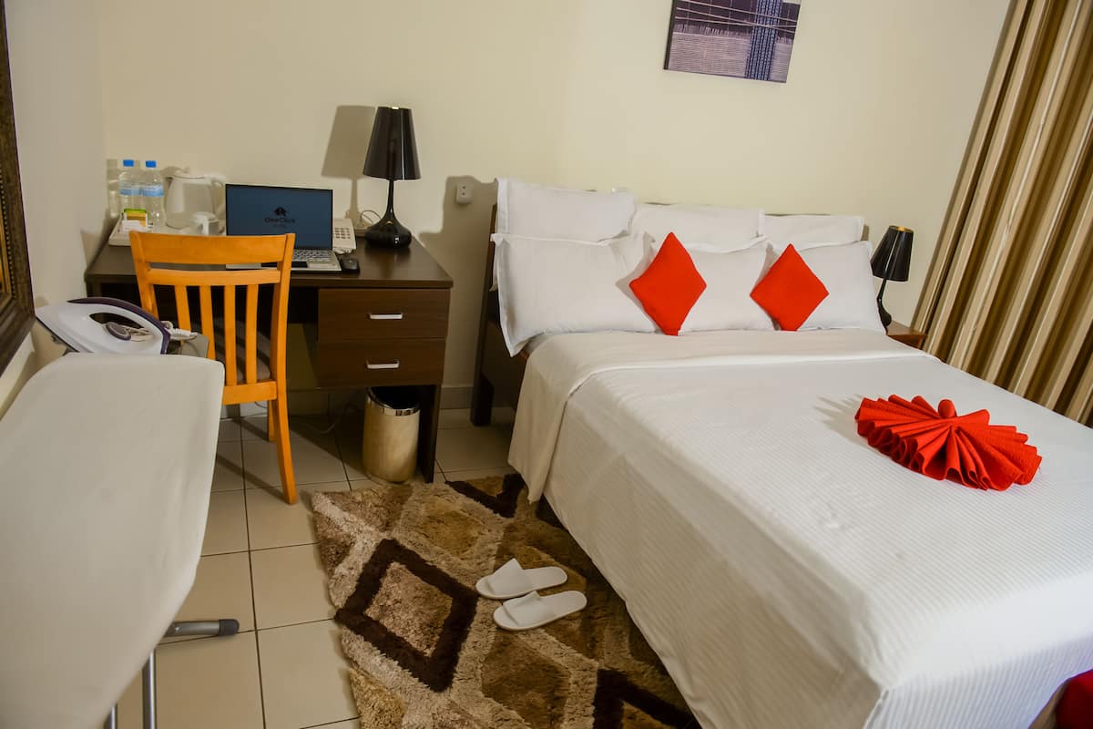 A hotel room with a bed, a desk with a laptop, a chair, and a small trash bin.