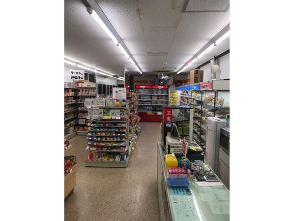 Un rayon d’épicerie avec des étagères remplies de divers produits, un espace réfrigéré et une zone de caisse.