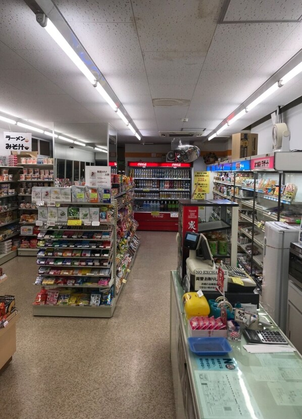 Un corridoio di un supermercato con scaffali pieni di prodotti diversi, una cassa e un reparto refrigerato.