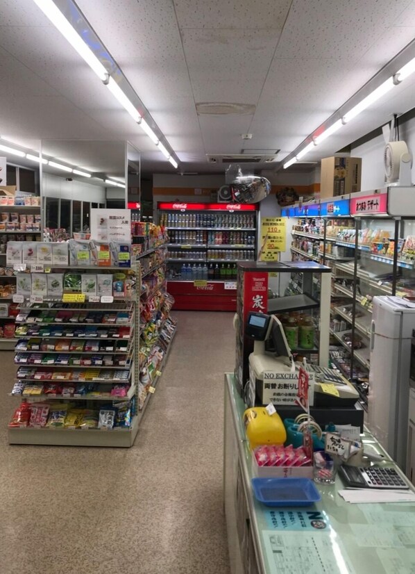 A grocery store aisle with shelves stocked with various products, a refrigerated section, and a checkout area.