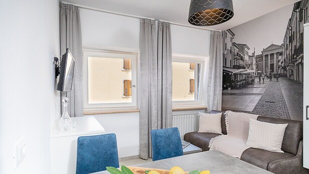 Een moderne woonkamer met een eettafel, blauwe stoelen, een bruine bank en een groot raam met gordijnen.