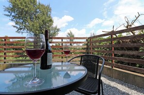 Relax in this serene outdoor seating area with a round table and wicker chair, perfect for enjoying a glass of wine.