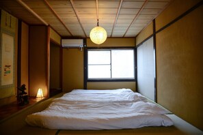 A traditional Japanese room with tatami flooring, a futon bed, a shoji screen window, and a hanging paper lantern.